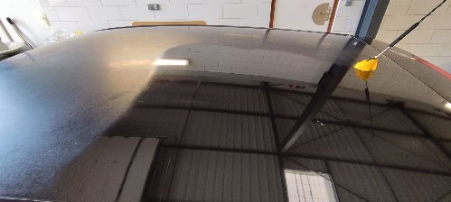 Toit d'une Volkswagen Polo après lustrage : la charpente de l'atelier se reflète dans la peinture