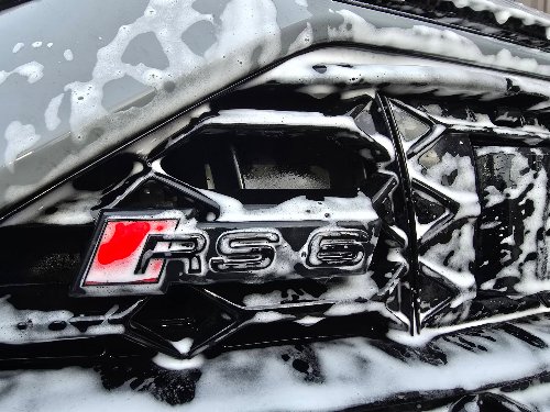 Calandre et logo RS6 d'une Audi couverts de mousse active pendant le prélavage