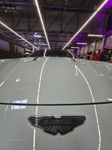 Capot et écusson d'une Aston Martin sous les éclairages : reflets nets après lustrage
